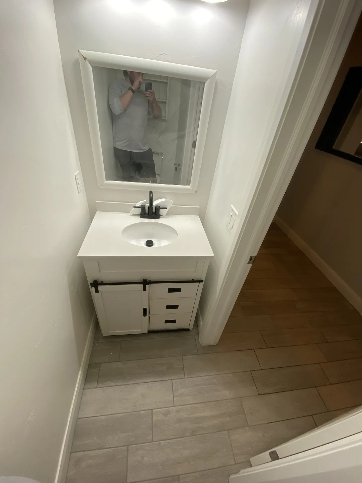 Finished bathroom floor in warm gray plank tile beside a white vanity with black hardware