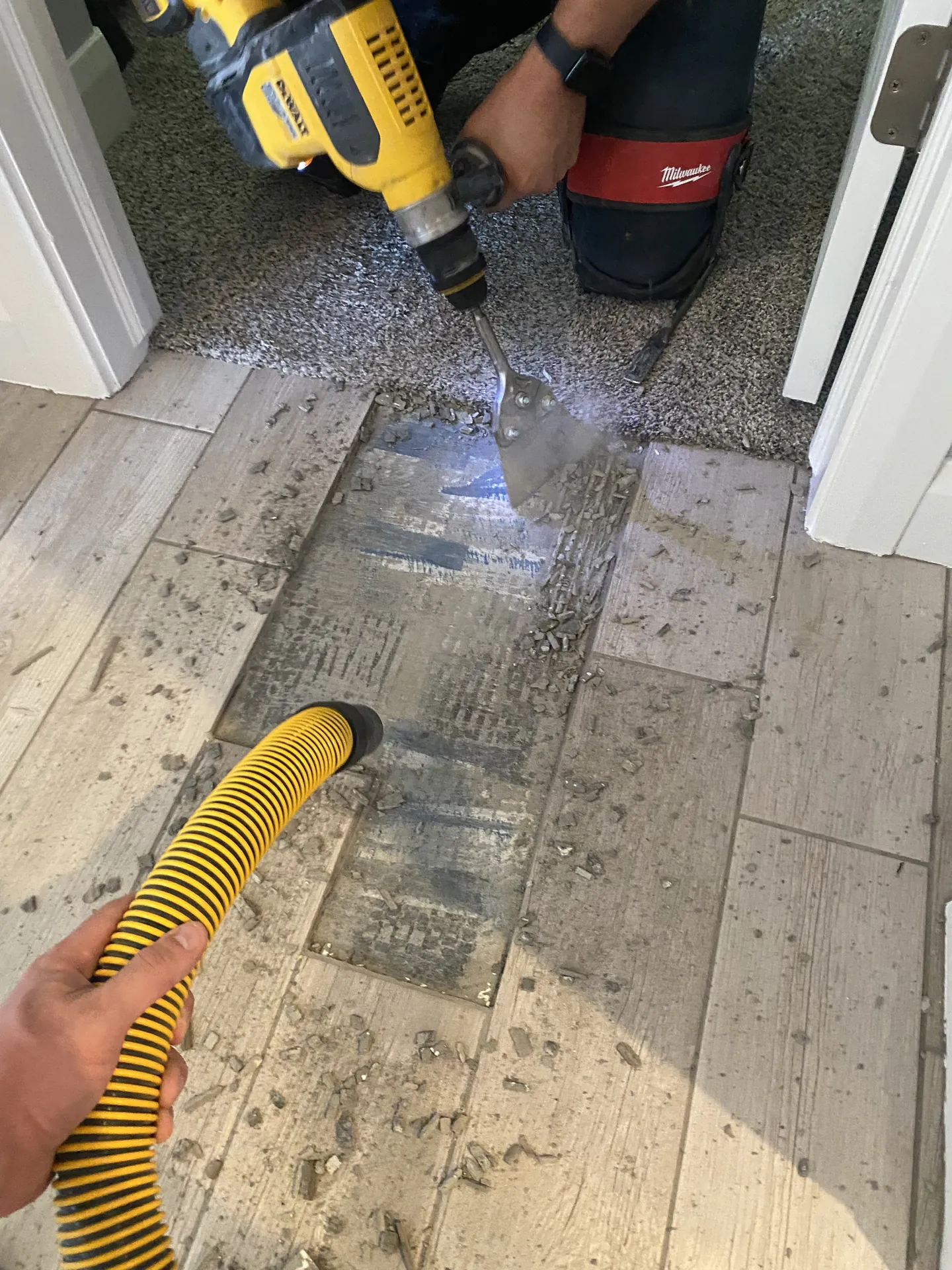 Close-up of a rotary hammer chisel lifting old tile off the subfloor with vacuum dust collection attached