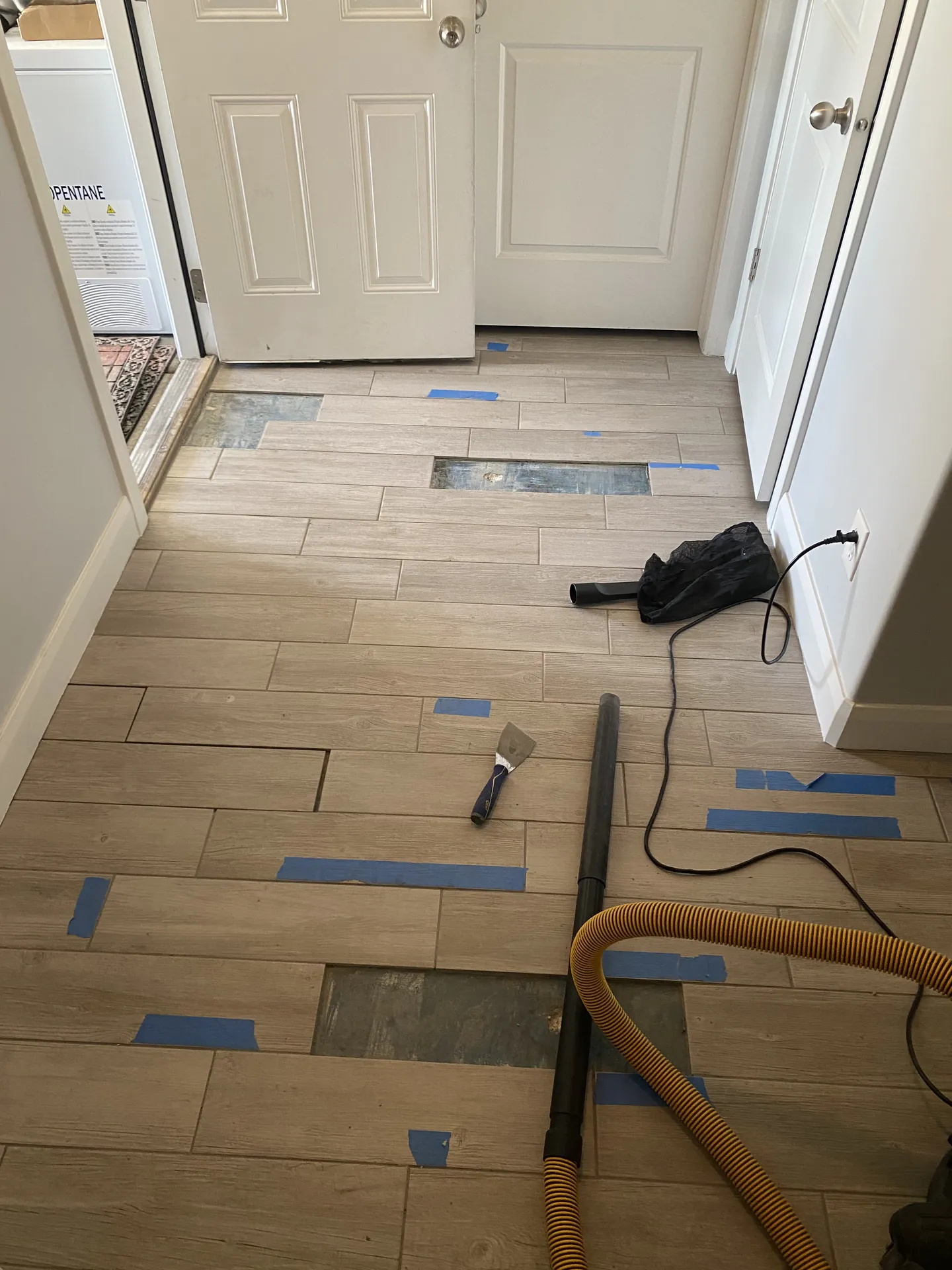 Wood-look plank tile installation in progress with blue layout tape holding the pattern across the entry