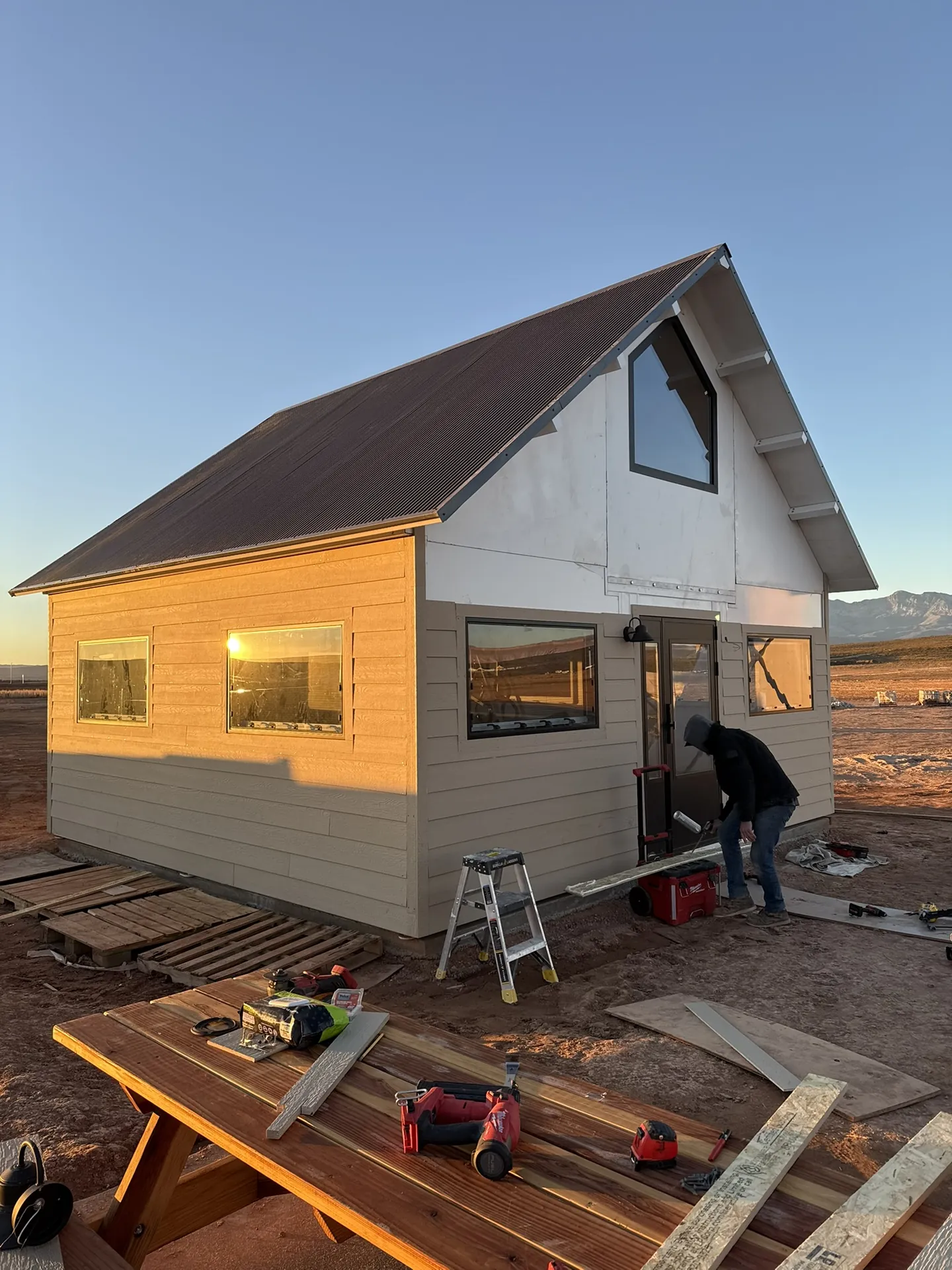 Lap siding partially installed on the Boxabl unit at golden hour with a crew member working at the front door