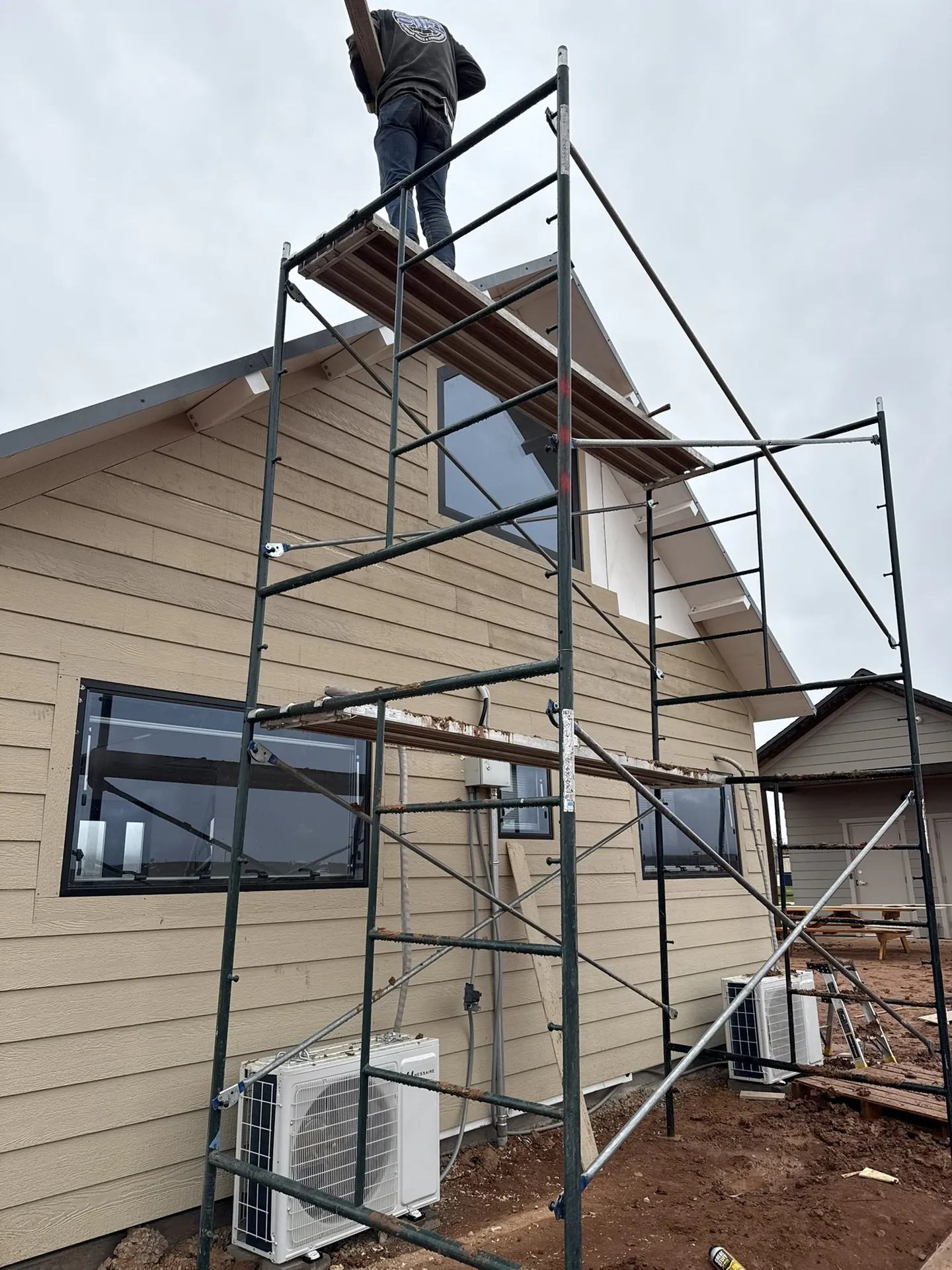 Crew on scaffolding installing upper siding courses on the Boxabl unit under an overcast sky