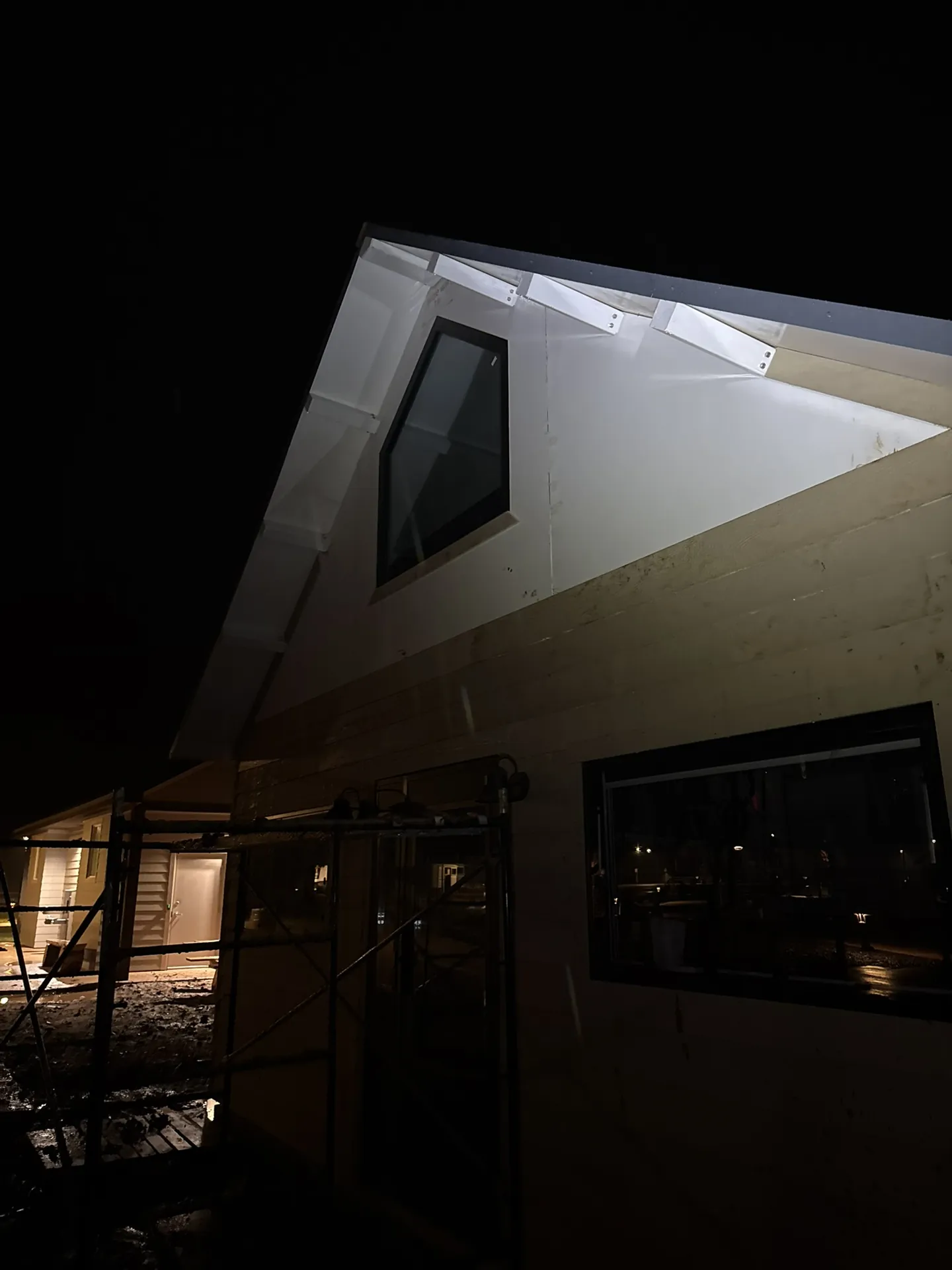 Boxabl unit lit up at night mid-install with scaffolding in place and mud at the base of the site