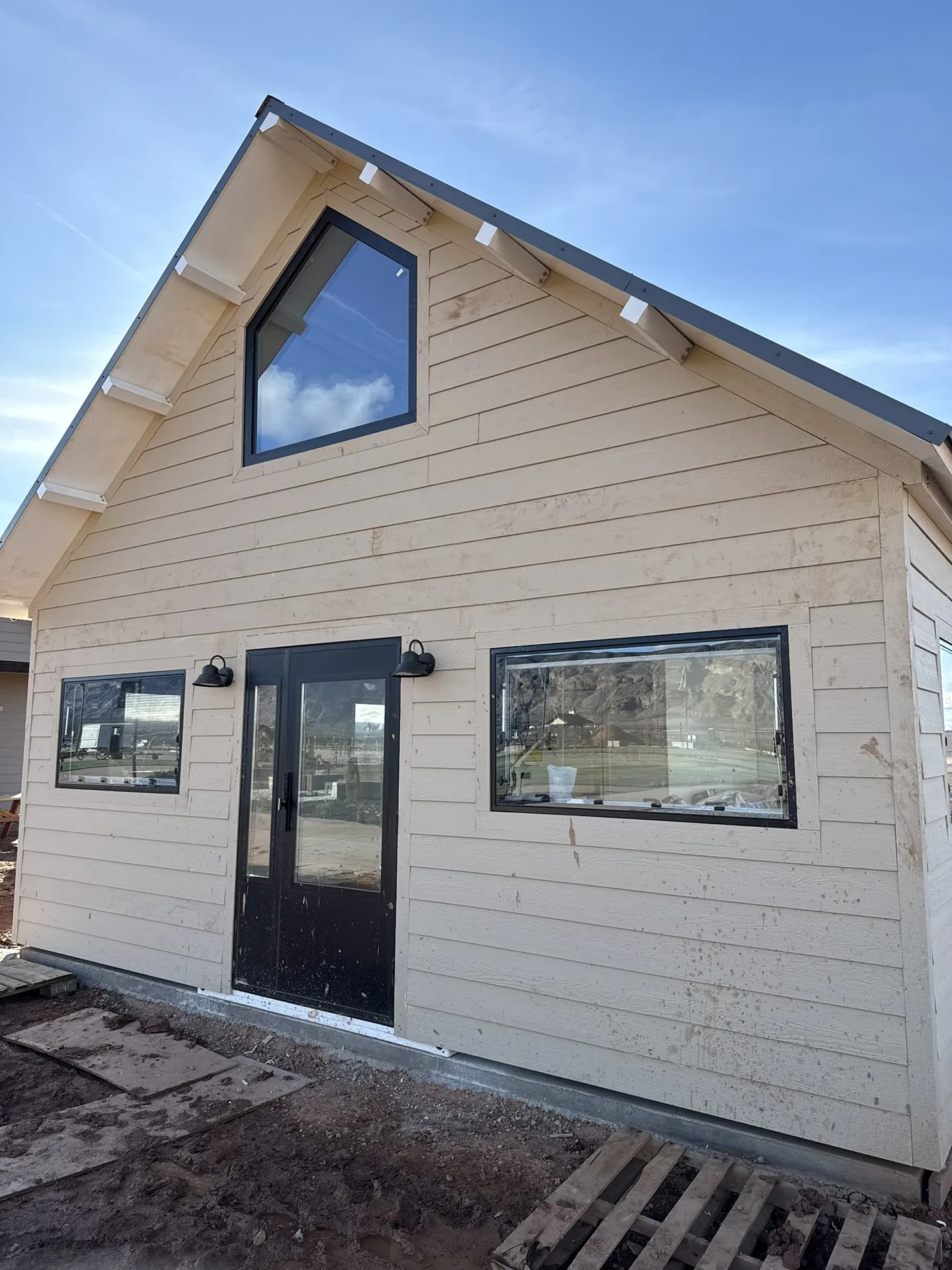 Completed front face of the sided Boxabl unit with black door, trimmed windows, and mounted exterior lights